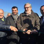 Gruppo di uomini in giacca e cravatta durante una cerimonia di inaugurazione all'aperto, tagliano un nastro verde.
