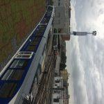 Treno blu su rotaie in una stazione sotto un cielo nuvoloso, edifici sullo sfondo.