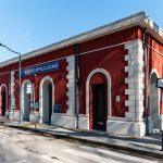 Edificio rosso delle Ferrovie Appulo Lucane con cielo sereno e segnaletica nelle vicinanze.