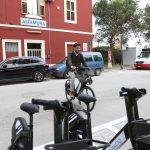 Ciclista urbano in bicicletta vicino alla stazione di Altamura, con auto e furgoni parcheggiati sullo sfondo.