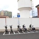 Parcheggio con biciclette condivise, sfondo di edifici e serbatoio d'acqua bianco.