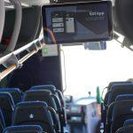 Alt text: Interno di un autobus con sedili blu e uno schermo che mostra l'app mobile di Ferrovie Appulo Lucane per informazioni sui viaggi.