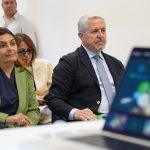 Partecipanti a un incontro, ascoltando presentazioni su un laptop in un ambiente professionale.