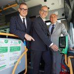 Tre uomini sorridenti a bordo di un autobus, mostrano il nuovo sistema di pagamento contactless.
