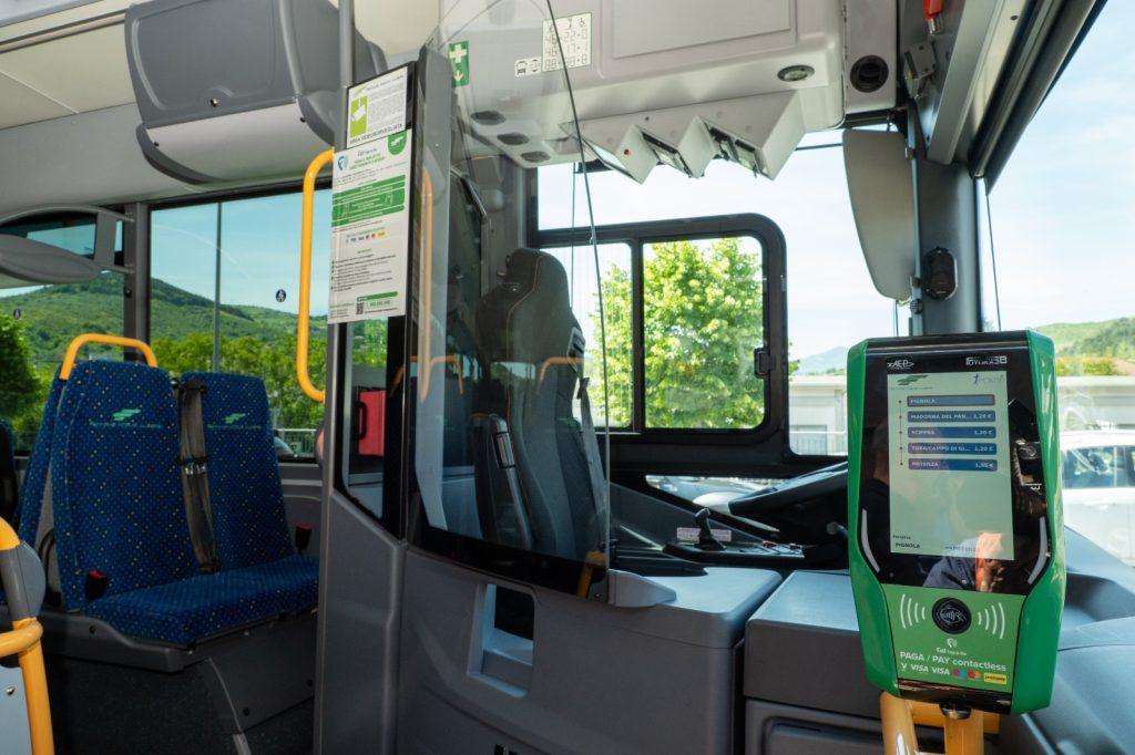 Interno di un autobus con posti a sedere e dispositivo di pagamento contactless visibile. Ambiente luminoso e moderno.