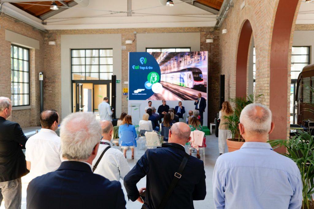 Evento di presentazione nel settore dei trasporti, con persone di spalle e schermo che mostra un treno innovativo.